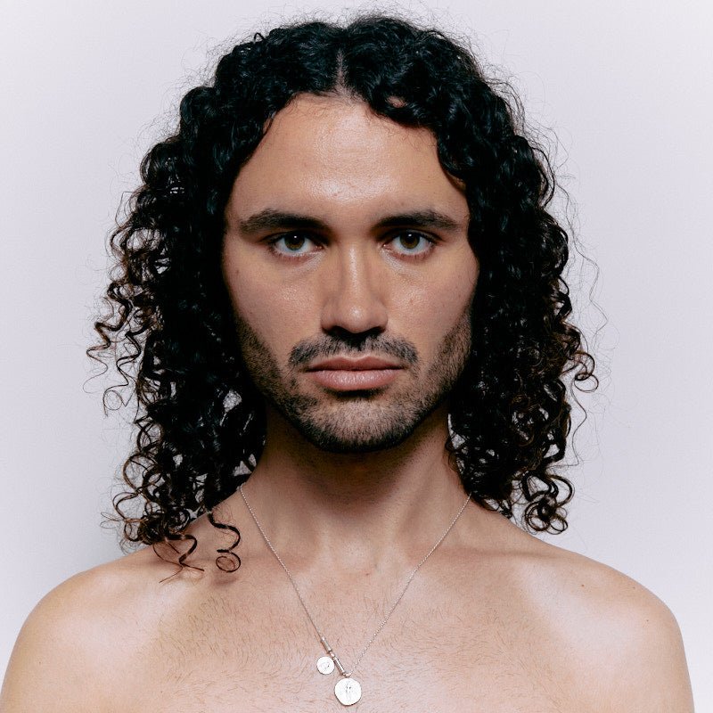Portrait of a model with curly hair wearing a sterling silver Angelus pendant necklace.